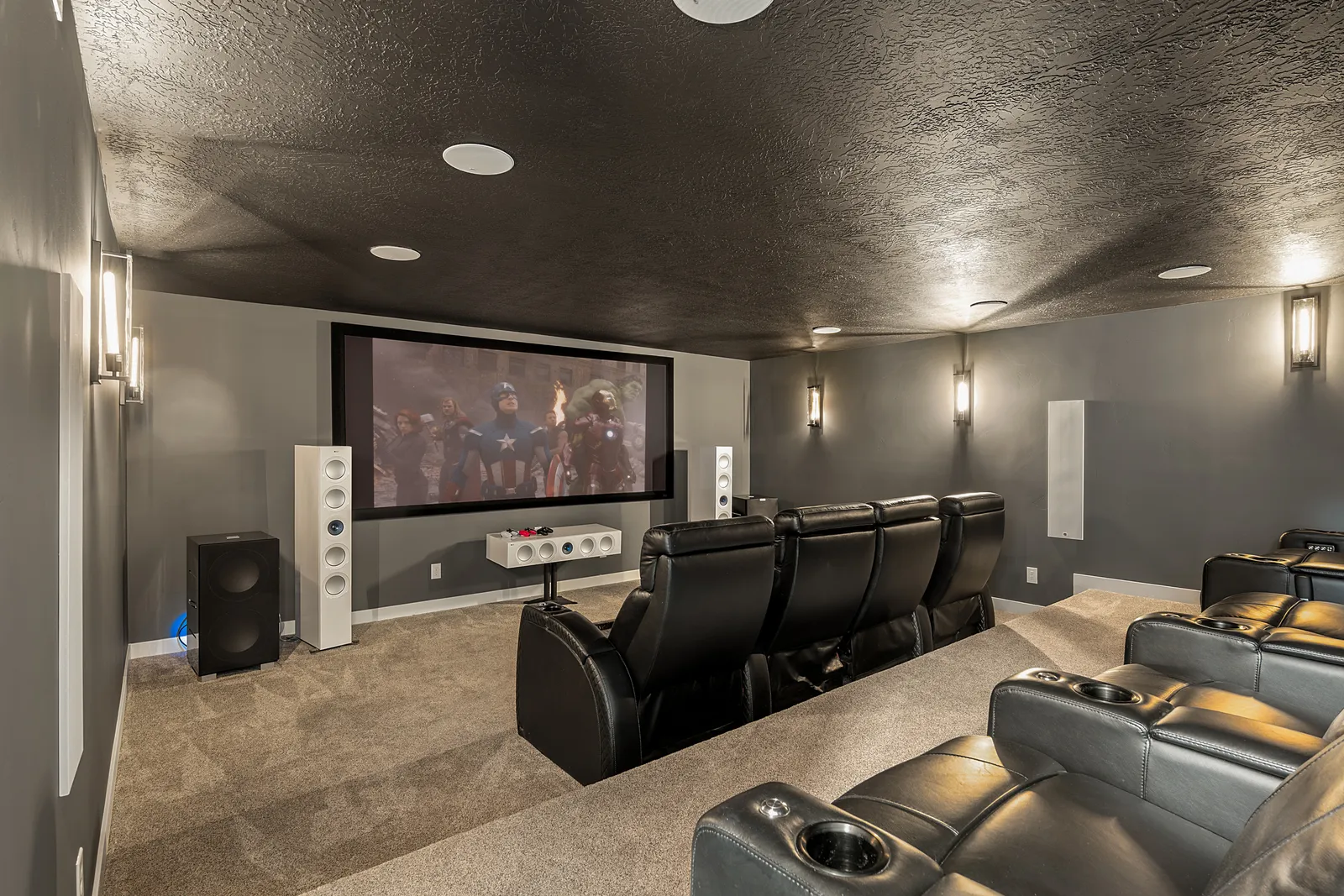 Finished home theater with the screen lit, tower speakers, and tiered leather seating